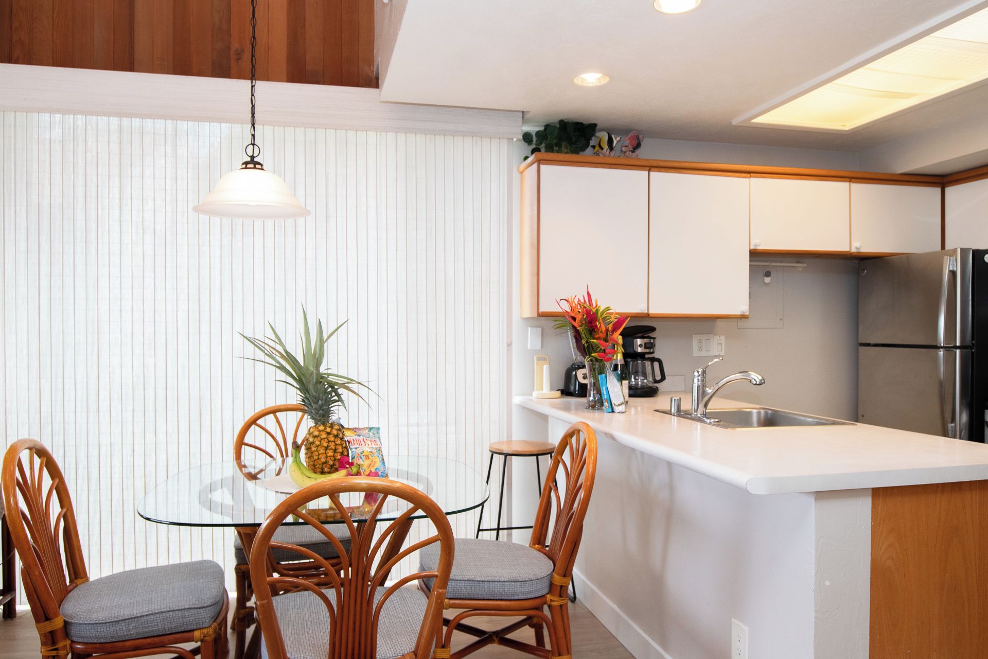 A modern kitchen with a central island, wooden chairs, and a hanging light fixture.