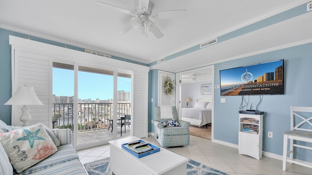 Un salon spacieux avec balcon, un téléviseur fixé au mur et une vue sur le paysage urbain.