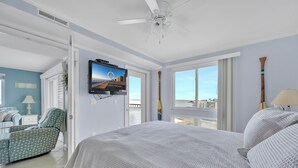 Une chambre à coucher avec un lit, une télévision, un ventilateur de plafond et une vue sur la ville grâce à de grandes fenêtres.