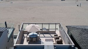 Blick auf einen Strand von einem Balkon mit Tisch und Stühlen, einem großen Sonnenschirm und Meerblick.