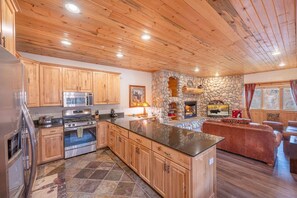A kitchen with wooden cabinets, a stone fireplace, and a large island.