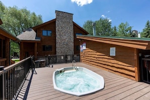 A wooden cabin with a hot tub on a deck, surrounded by trees.