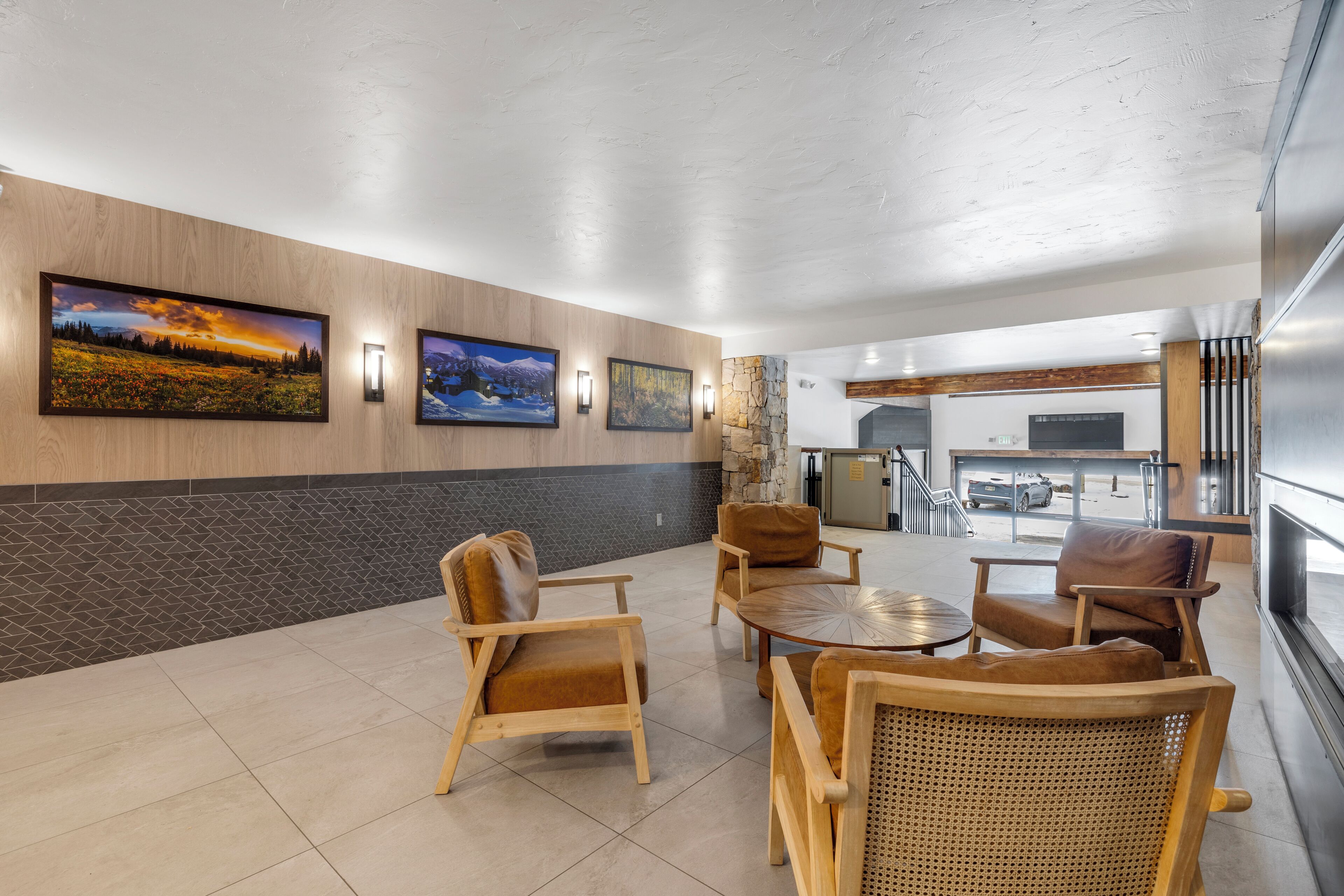 Eine moderne Lobby mit Wandverkleidungen aus Holz und Stein, einem Kamin und einer Sitzecke mit Ledersesseln und Korbmöbeln.