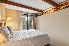 A bedroom with a bed, a window with curtains, a lamp, and a painting on the wall.