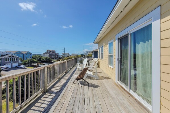 Une terrasse en bois avec une chaise, une porte vitrée et une vue sur un quartier résidentiel.