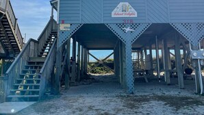 A beach house with a covered porch, a staircase leading to the entrance, and a sign indicating 'Island Delights'. - Island Delights II – Sun, Sand & Simple Fun (Surf City)