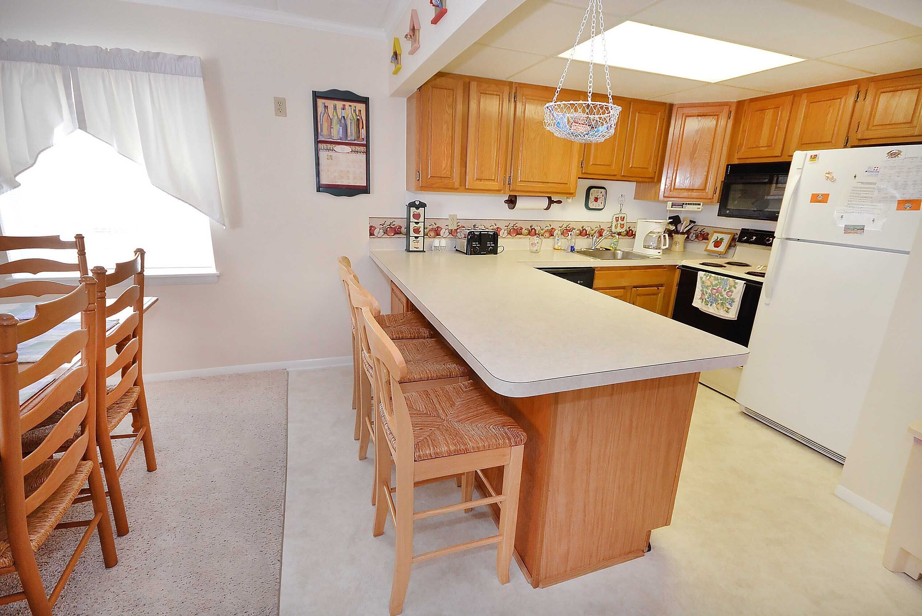 A kitchen with wooden cabinets, a white refrigerator, a microwave, and a sink. There are wooden chairs and a small island with a sink.