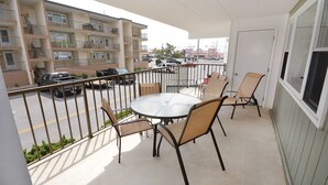 Un balcón con una mesa redonda y sillas, vista a un estacionamiento y un edificio de varios pisos con balcones.