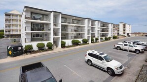Un edificio residencial de varios pisos con balcones, estacionamiento y cielo despejado.