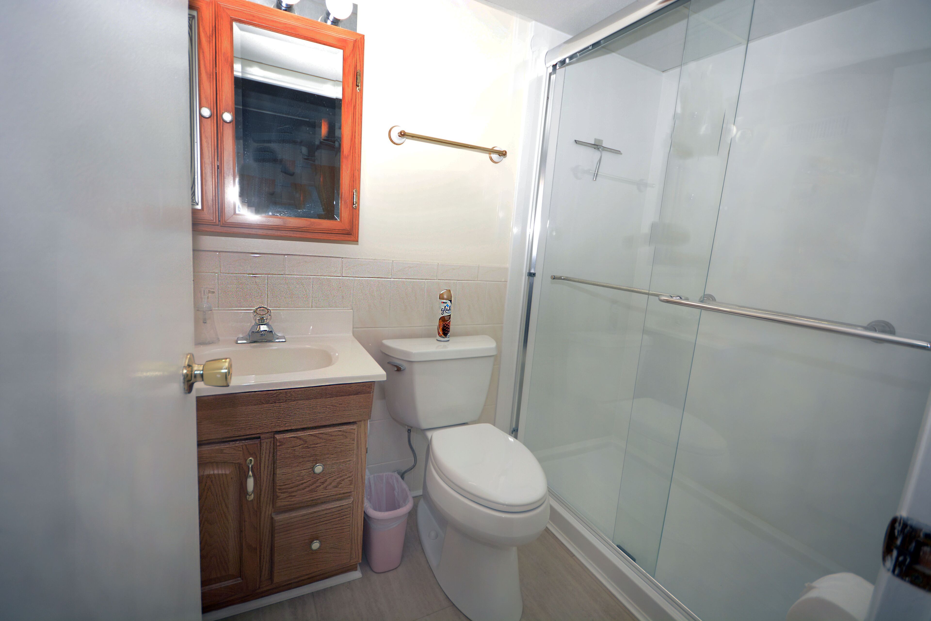 Un baño con un mueble de madera, un lavabo blanco, un inodoro y una cabina de ducha de vidrio.
