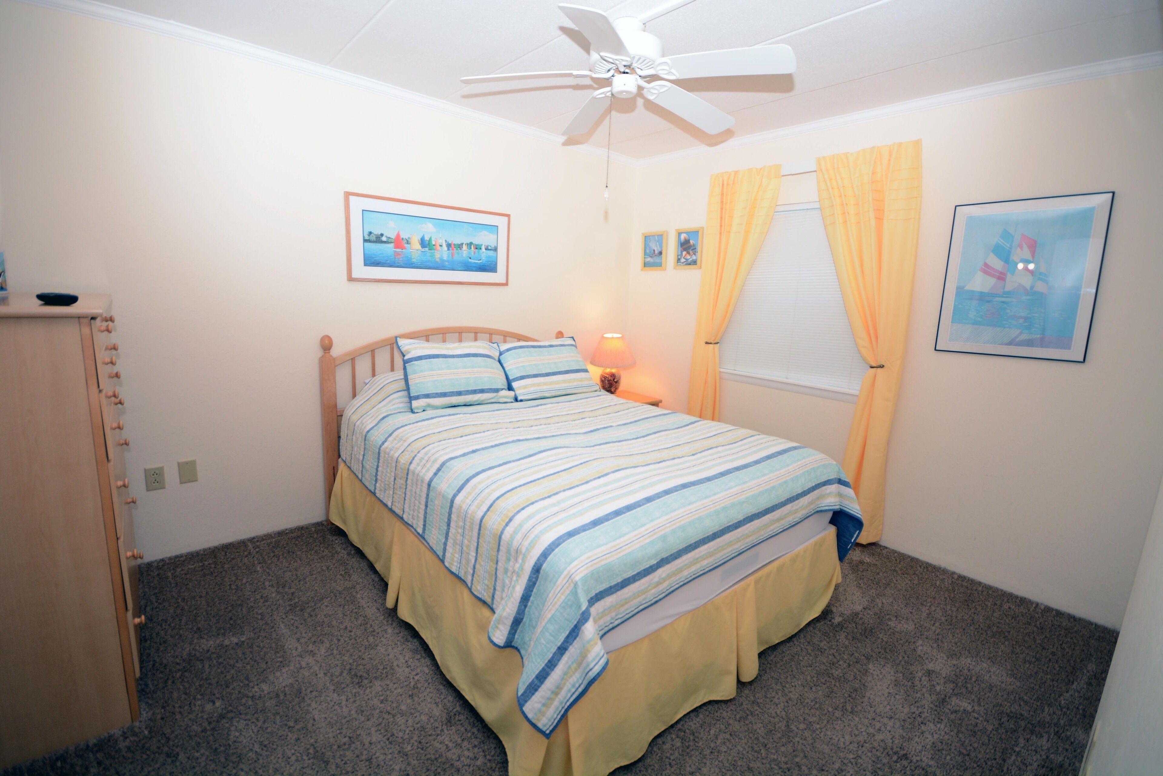 Une chambre à coucher avec un lit, un ventilateur de plafond, une table de chevet et une fenêtre avec des rideaux.
