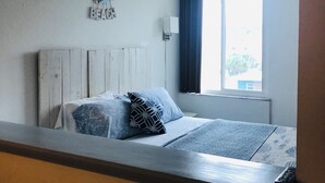 Un dormitorio con cama, ventana con cortinas, aire acondicionado de pared y un letrero decorativo.