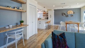 Een moderne keuken met witte kasten, houten planken en een eethoek met een tafel en stoelen.