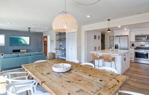 Une cuisine moderne avec des meubles blancs, un îlot central et un coin repas comprenant une table en bois et des chaises blanches.