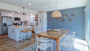 Een moderne keuken met witte kasten, een houten eiland en een eetgedeelte met een houten tafel en witte stoelen.
