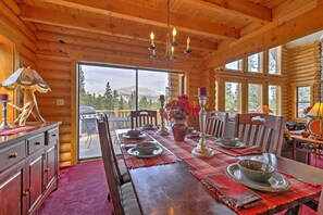 Interieur van een houten chalet met een eettafel gedekt voor vier personen, een kroonluchter en uitzicht op de omgeving.