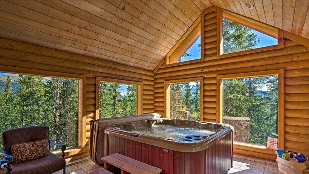 Eine Holzhütte mit Whirlpool, Holzbanken und großen Fenstern mit Blick auf den Wald.