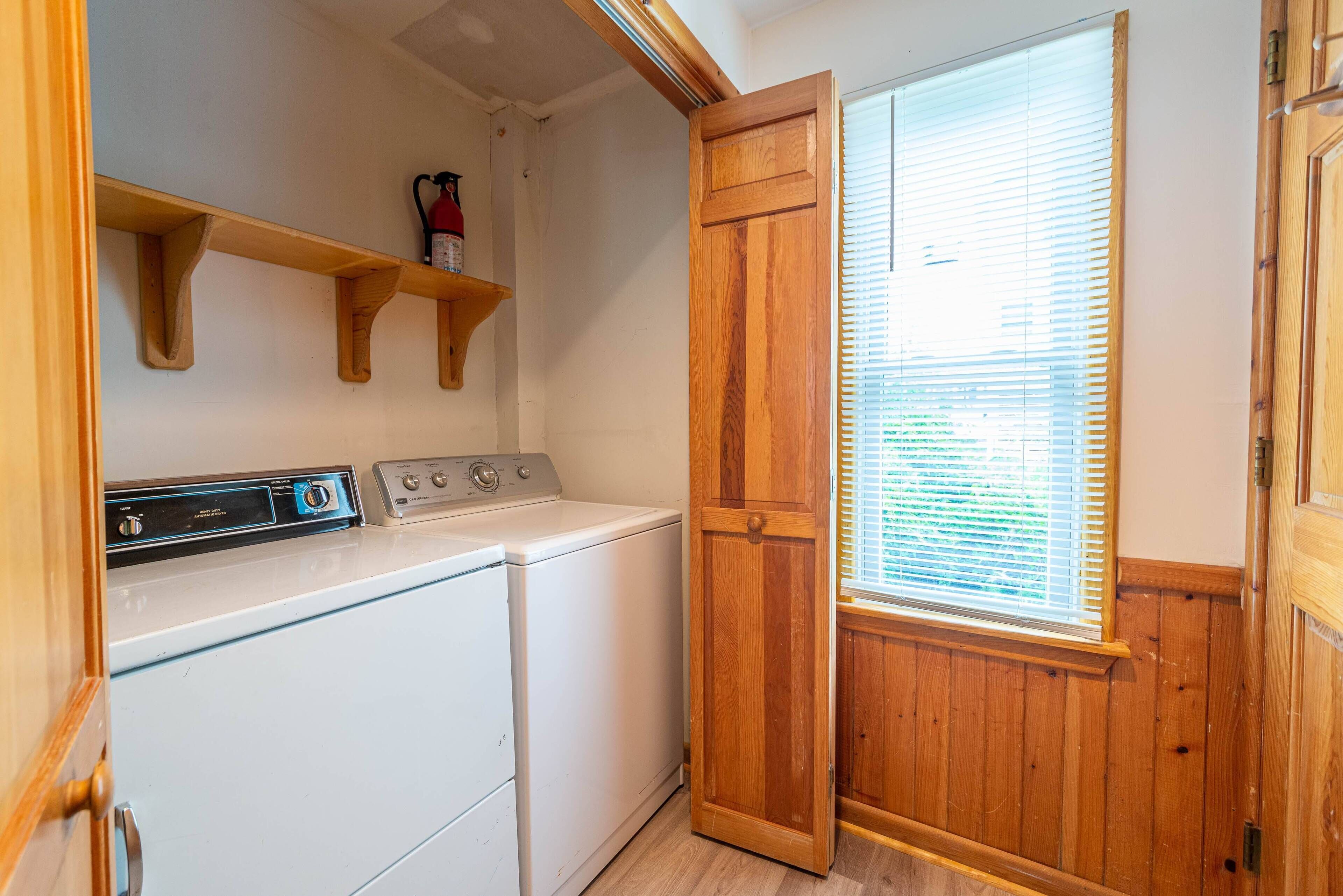 A laundry room with a white washer and dryer, wooden shelves, and a wooden door.
