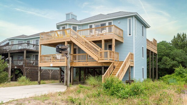 Ein zweigeschossiges Haus mit einer Holzterrasse und einer Treppe, die zu einem Balkon führt.
