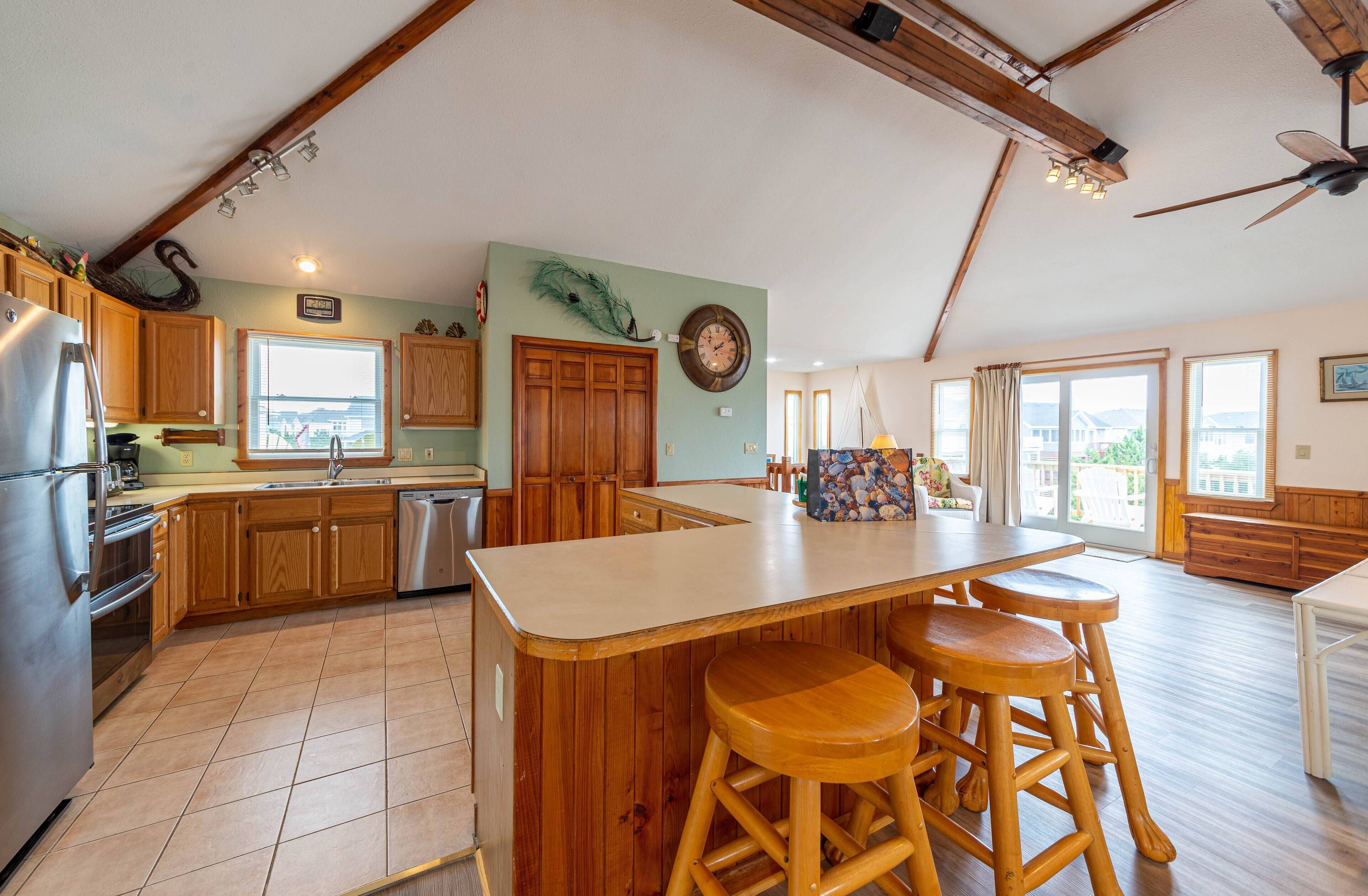 A spacious kitchen with wooden cabinets, a large island with stools, a built-in oven, and a view of the outside.
