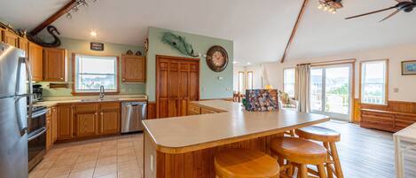 A spacious kitchen with wooden cabinets, a large island with stools, a built-in oven, and a view of the outside.