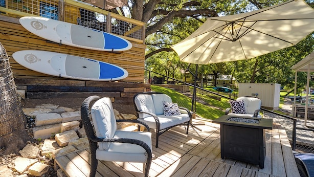 A wooden deck with two white cushioned chairs, a small table, and a surfboard rack. - Waterfront Lake LBJ Cabin w/ Private Dock! (Burnet)