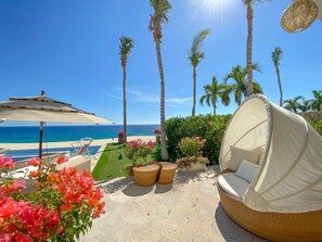 Relax in a serene ocean-view seating area with a wicker sofa, lounge chair, and small table surrounded by palm trees.