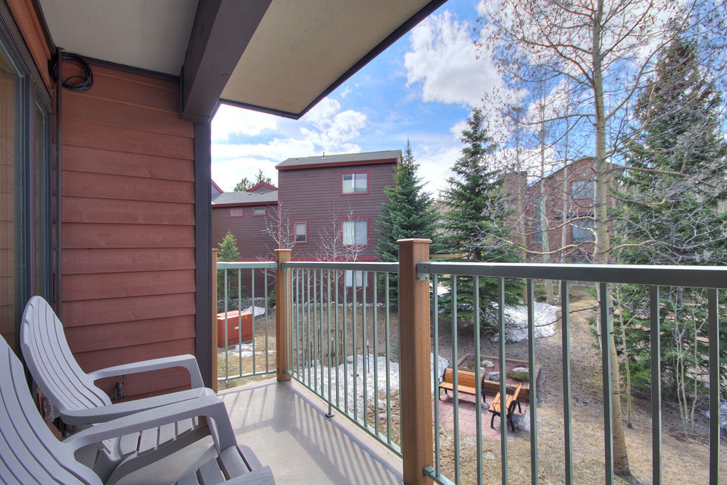 Un balcon avec deux chaises blanches, un banc en bois et une rambarde en métal.
