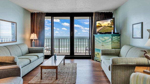 A living room with a view of the ocean, a sofa, a coffee table, and a cabinet with a painting.