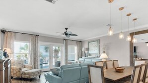 Ein geräumiger Wohnbereich mit einer Couch, einem Esstisch und Stühlen. Ein Deckenventilator und Pendelleuchten sind vorhanden.