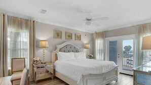 Ein Schlafzimmer mit einem großen Bett, zwei Nachttischen, einem Sessel, einem Deckenventilator und einer Tür, die auf einen Balkon führt.
