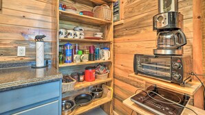 A kitchen with wooden shelves holding various kitchenware, a coffee maker, and a toaster oven. - 'Sardis Serenity' 1 BR Clayton Cabin w/ Lake View (Clayton)
