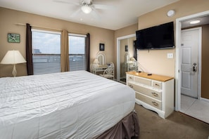 A bedroom with a bed, dresser, vanity, and a television.