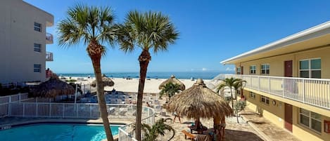 Ett semesterparadis med en swimmingpool, palmer, strandparasoller och utsikt över havet.