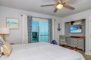 A bedroom with a bed, a ceiling fan, a TV, a dresser, and a window with curtains.