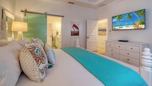 Un dormitorio con cama, televisor, cómoda y una puerta que da a otra habitación.