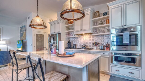 Una cocina moderna con armarios blancos, electrodomésticos de acero inoxidable y una isla central con taburetes de bar.