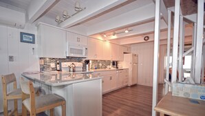 Una cucina moderna con mobili bianchi, un'isola centrale e un forno a microonde. Sono presenti sedie di legno e un tavolo con un portatovaglioli.