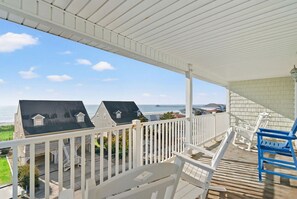 A covered porch with a view of the ocean, white railings, and a blue chair.