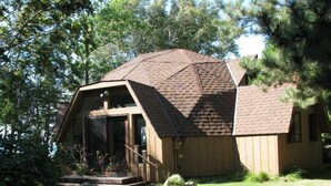 Uma cabana com telhado inclinado, varanda frontal e uma janela grande.