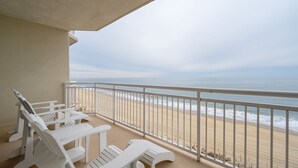 Un balcón con sillas Adirondack blancas que da a una playa.