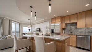Una cocina moderna con una isla central, taburetes de bar, electrodomésticos de acero inoxidable y armarios de madera.