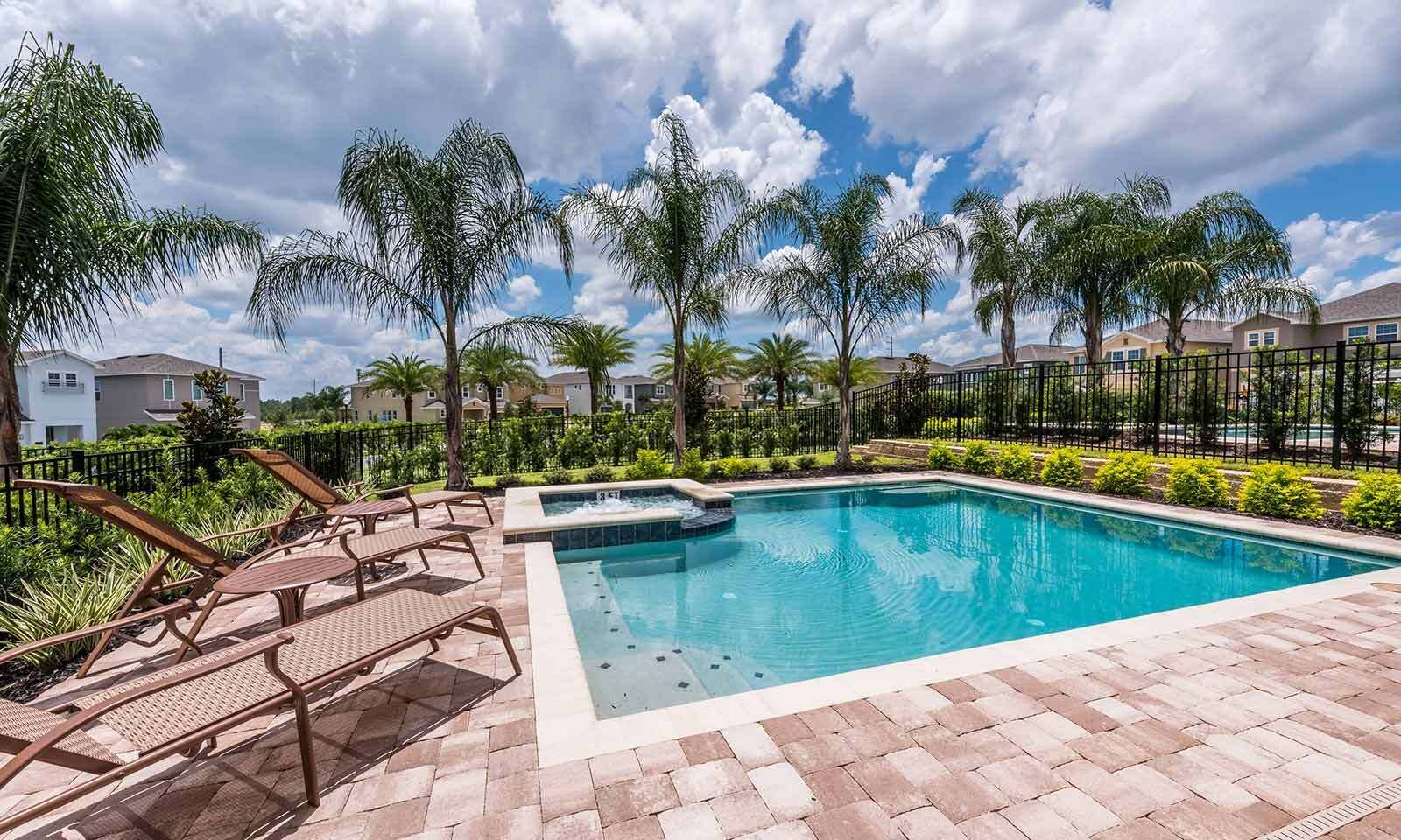 A swimming pool with lounge chairs, surrounded by palm trees and a brick patio.