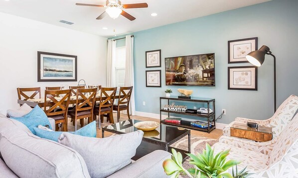 A living room with a sofa, coffee table, TV, and a dining area with chairs and a table. - 6-Bedroom Luxury Vacation Home at Encore Resort | Private Pool & Spa (Kissimmee)