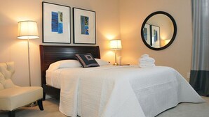 Ein Hotelzimmer mit einem Bett, zwei Nachttischlampen, einem Sessel, einem runden Spiegel und zwei gerahmten Bildern an der Wand.