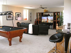 A living room with a pool table, a bar area, a television, and a ceiling fan. - 'The Key West' Las Vegas House w/ Private Pool! (North Las Vegas)