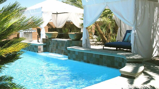Ein Pool mit Wasserfall, umgeben von Palmen und überdachten Sitzbereichen.