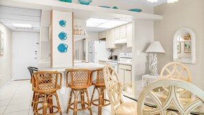 Una cocina moderna con gabinetes blancos, una isla central con taburetes y decoración de peces azules en la pared.