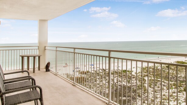 Un balcón con sillas de mimbre, una mesa y vista a la playa y al océano.