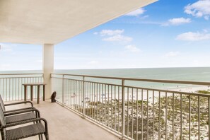 Varanda com cadeiras de vime, uma mesa e vista para a praia e o oceano.